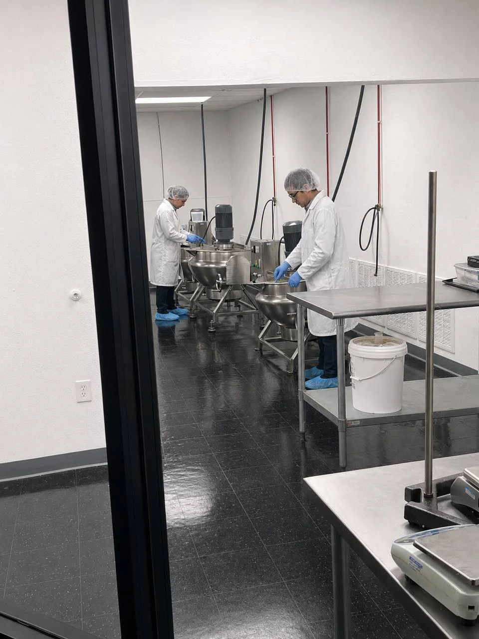 GIH production team working with stainless kettle equipment viewed through glass
